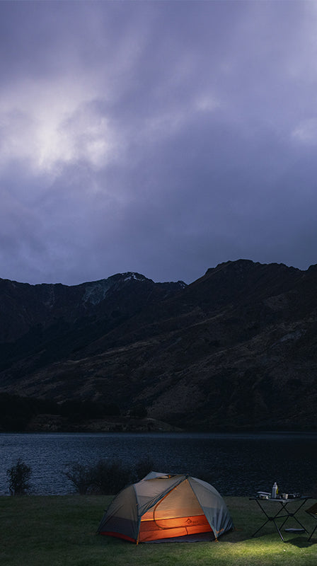 Camping scene with a tent, car, and mountains under a dark sky.